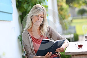 Mature woman reading book and drinking coffee