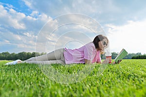 Mature woman reading book, female lying on green grass with drink