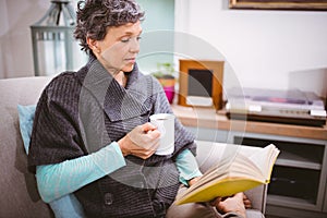 Mature woman reading book and holding coffee mug