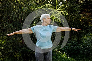 Mature woman relaxing in nature. Old woman meditating. Senior woman is doing yoga in the park.