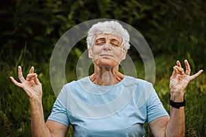 Mature woman relaxing in nature. Old woman meditating. Senior woman is doing yoga in the park.