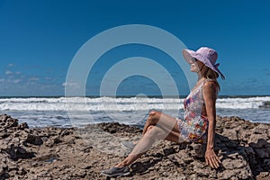 Mature woman relaxing outdoors sitting on the rocks near the sea.