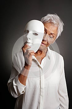 Mature woman revaling sad face behind mask photo