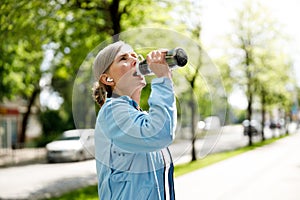 Mature Woman Runner Drinking From the the Sport Bottle After Training on the Blurred Background. Sport and Healthy