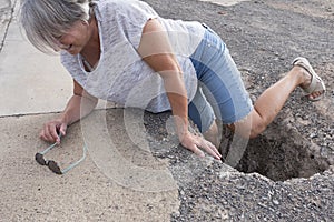 Mature woman or senior walking in a building zone and falling in a big hole with her leg inside it - needing help on the ground