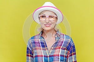 Mature woman in shirt, hat and eyeglasses, being in good mood, smiling broadly and winking at camera