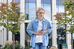 Mature woman in a shirt is walking in the city, a worker has a severe stomach ache, a blonde businesswoman in casual