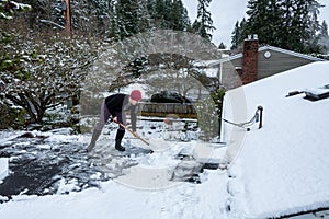 Mature woman shoveling fresh wet snow off a flat carport roof