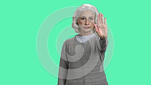 Mature woman showing stop gesture on turquoise background.