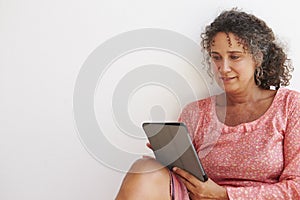 Mature Woman Sitting Against Wall Using Digital Tablet