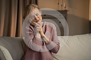 Mature Woman Sitting on Couch With Expression of Discomfort Due to Toothache