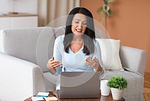 Mature woman sitting on couch, having video call on computer