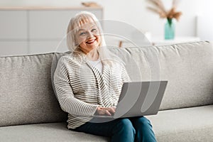 Mature woman sitting on couch and working on computer