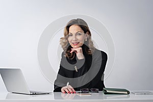 Mature woman sitting at desk and using laptop against isolated background
