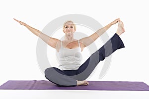 Mature woman sitting on mat and doing yoga with arms outstretched