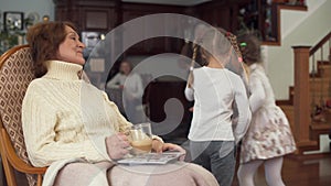 Mature woman sitting in a rocking chair and her small cute granddaughters came to her to kiss and gently hug