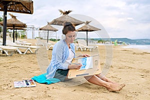 Mature woman sitting on sandy beach drawing sketch of sea