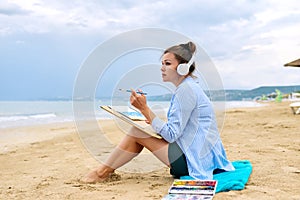 Mature woman sitting on sandy beach drawing sketch of sea