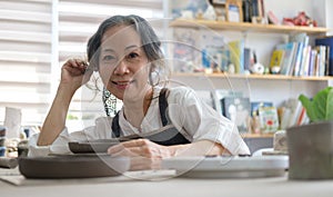 Mature woman small business owner sitting in handmade craftsmanship retail store and smiling at camera