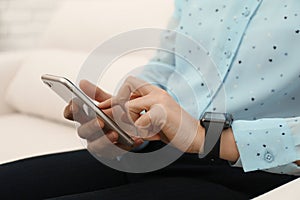 Mature woman with smart watch and phone indoors, closeup