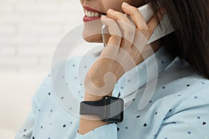 Mature woman with smart watch talking on phone indoors, closeup