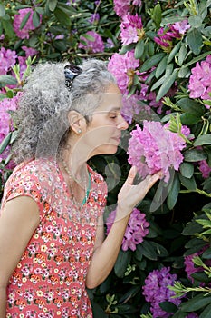 Mature woman smelling on flowering Rhododendron bush
