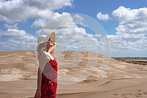 Mature woman smiling while enjoying relaxing in the sun on a sand dune. Summer concept.