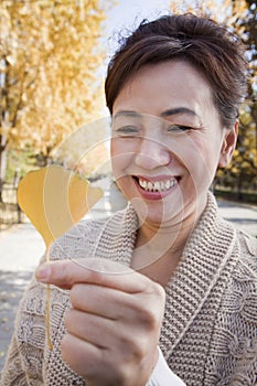 Mature Woman Smiling and Holding Yellow Ginkgo Leaf