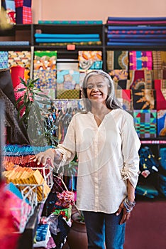 Mature woman smiling while working in her textiles shop