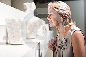 Mature woman standing in art museum near the antique sculpture