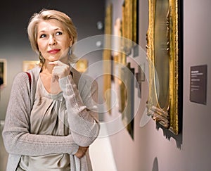 Mature woman standing in art museum near the painting in baguette