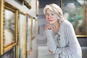 Mature woman standing in art museum near the painting in baguette