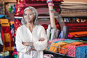 Mature woman standing in her colorful fabric and clothing shop