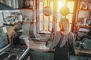 Mature woman standing next to a window in an old narrow cluttered kitchen