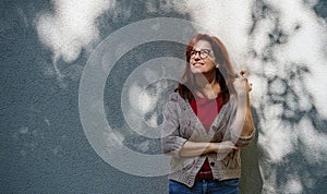 Mature woman standing outdoors in city or town against gray wall.