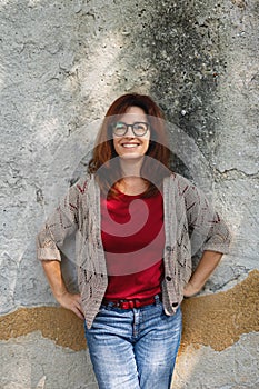 Mature woman standing outdoors in city or town against gray wall, looking at camera.