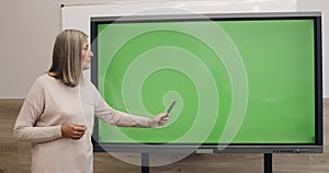 Mature woman with stylus pen talking and using interactive screen with template mock up screen. Female teacher