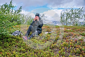 Mature woman takes rest pause and eats double sandwich. Hiking high in Norwegian mountains. Healthy lifestyle. Norway, Krutvatnet