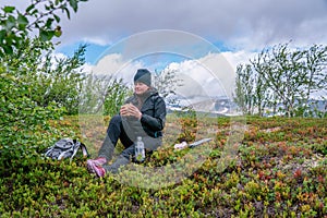 Mature woman takes rest pause, looking at double sandwich after first bite. Hiking high in Norwegian mountains. Healthy lifestyle