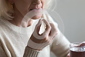 Mature woman taking pill holding glass of water, closeup view