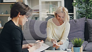 Mature woman talking to female psychologist sitting on couch in modern office