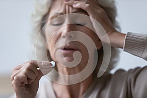 Mature woman touch forehead suffers from headache holding painkiller drug