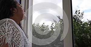 Mature woman touching her wet hair, looking out window and getting fresh air