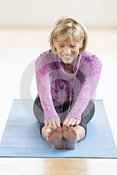 Mature Woman Touching Toes On Yoga Mat