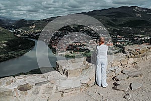 Mature woman tourist takes pictures on observation deck confluence of two rivers Aragvi and Kura, ancient city Mtskheta