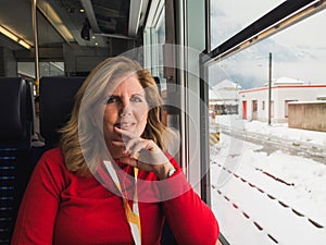 Mature woman traveling by train in winter snowy landscape looking out the window