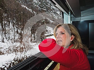 Mature woman traveling by train in winter snowy landscape looking out the window