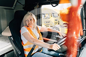 Mature woman truck driver steering wheel inside lorry cabin. Happy middle age female trucker portrait