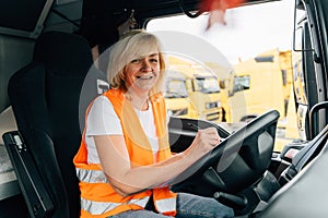 Mature woman truck driver steering wheel inside lorry cabin. Happy middle age female trucker portrait