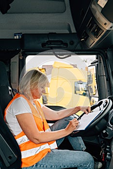 Mature woman truck driver steering wheel inside lorry cabin. Happy middle age female trucker portrait